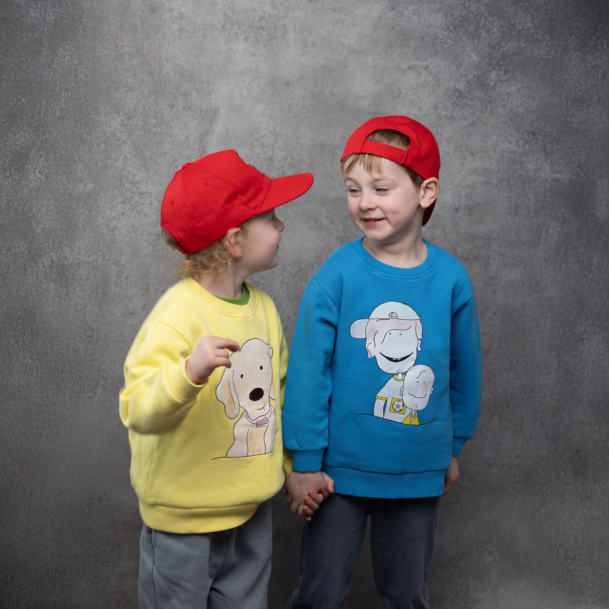 Two kids wearing children's Sweatshirts in Yellow Organic Cotton with Golden Retriever Print on the front and Blue with two cartoon children print on the front